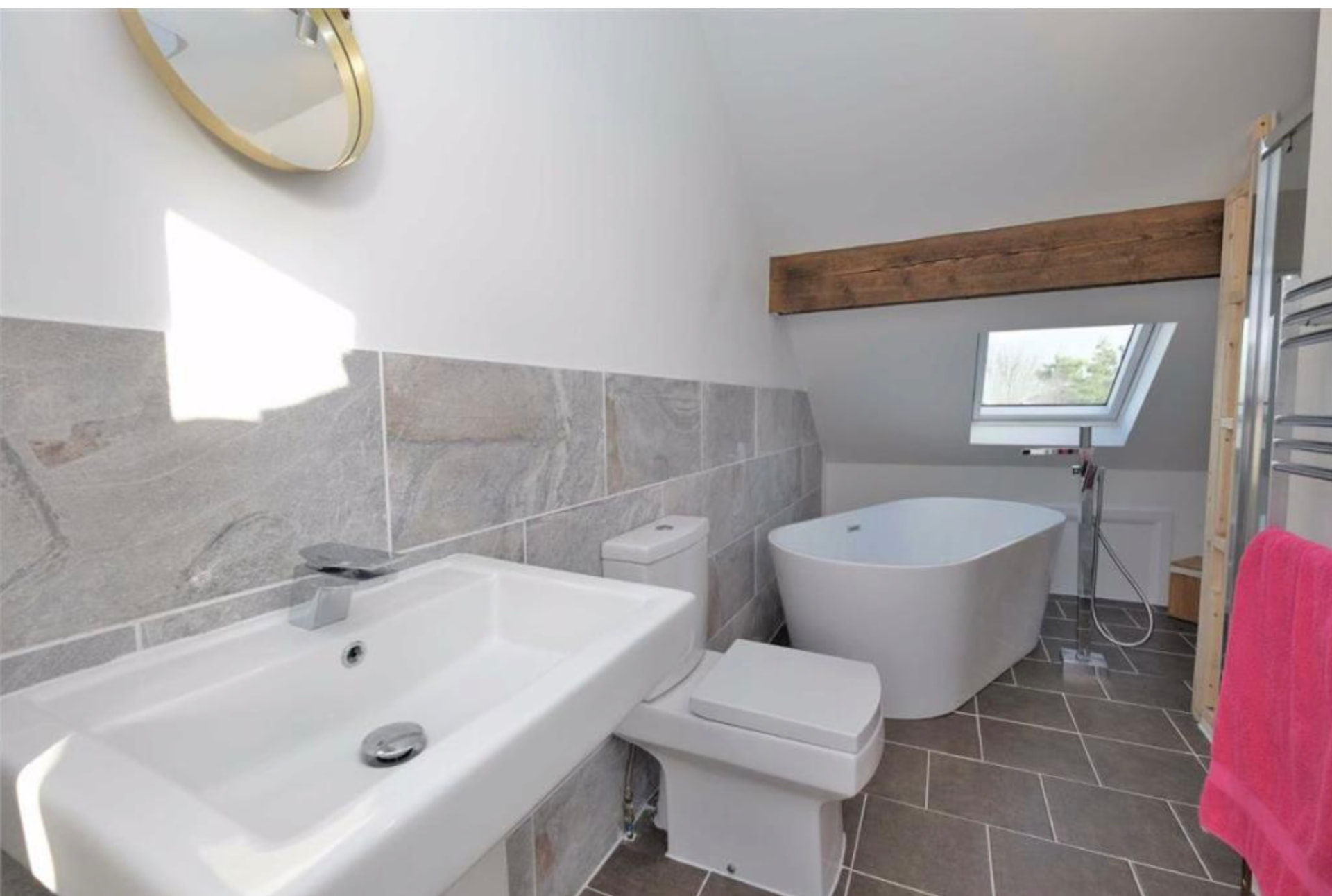 Finished loft bathroom with freestanding bath, rooflight and grey tiled floor
