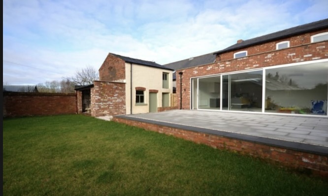 Single storey rear extension with brick walls, full-height sliding doors and a paved terrace opening onto the garden